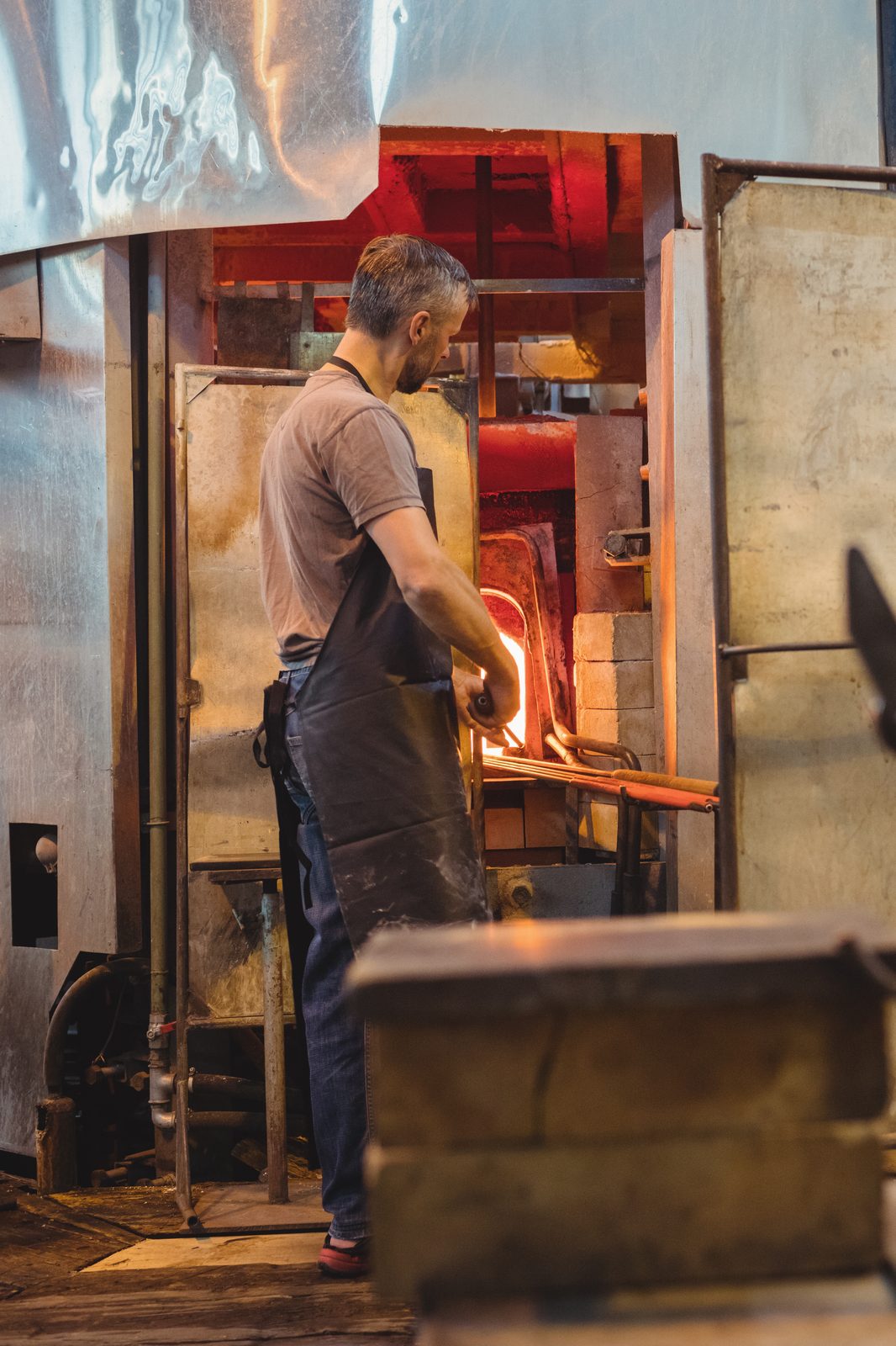 A glassmaker at an open furnace, heating glass on a blowpipe.