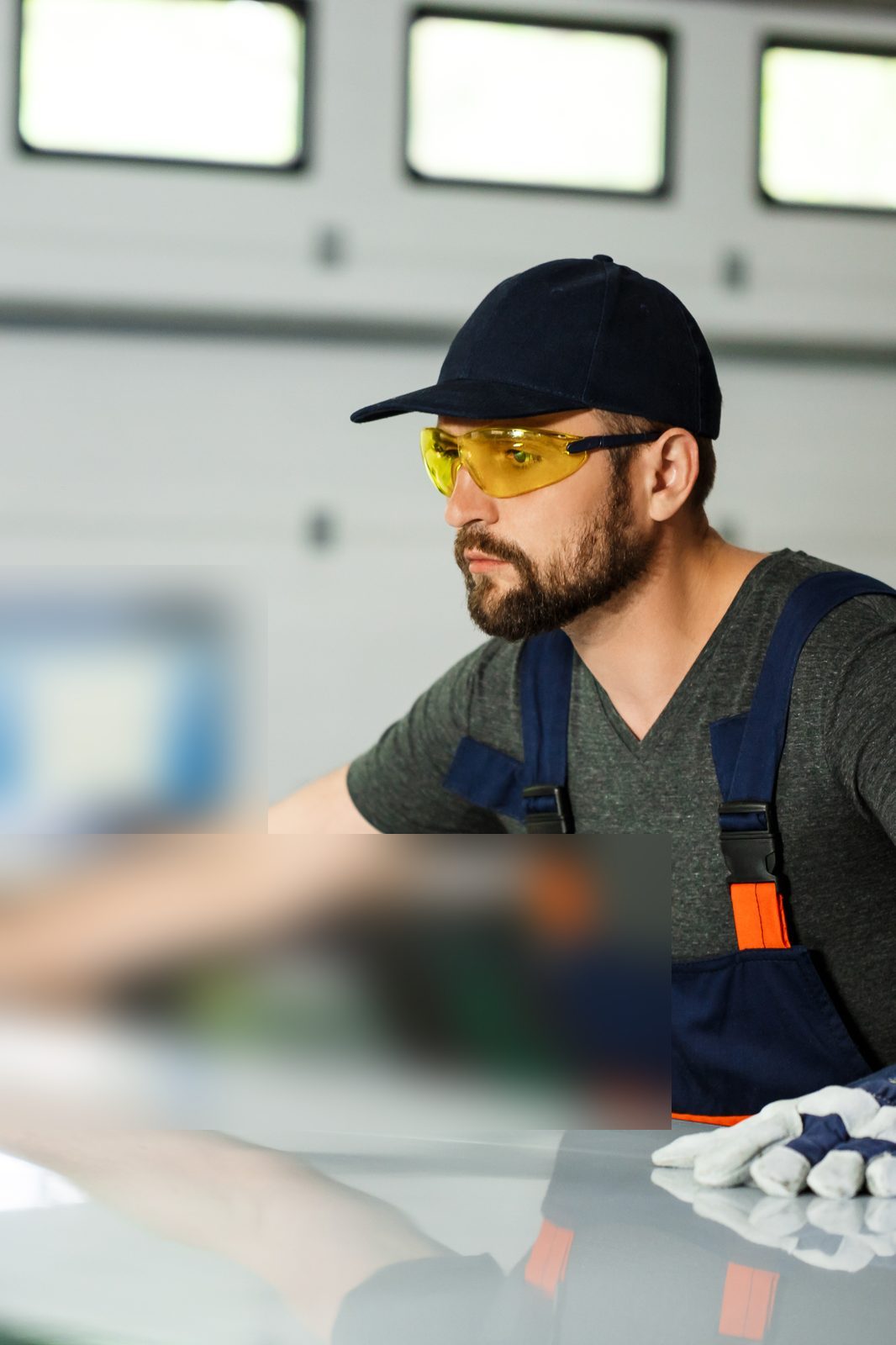 A worker in safety glasses and gloves checking a glass sheet.