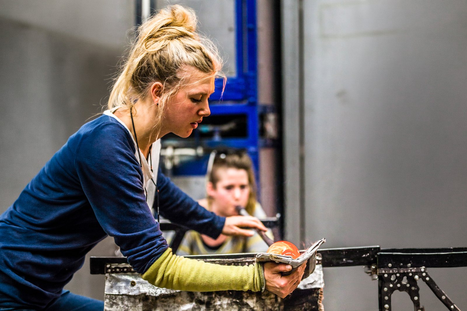 Two women shaping molten glass on a blowpipe.