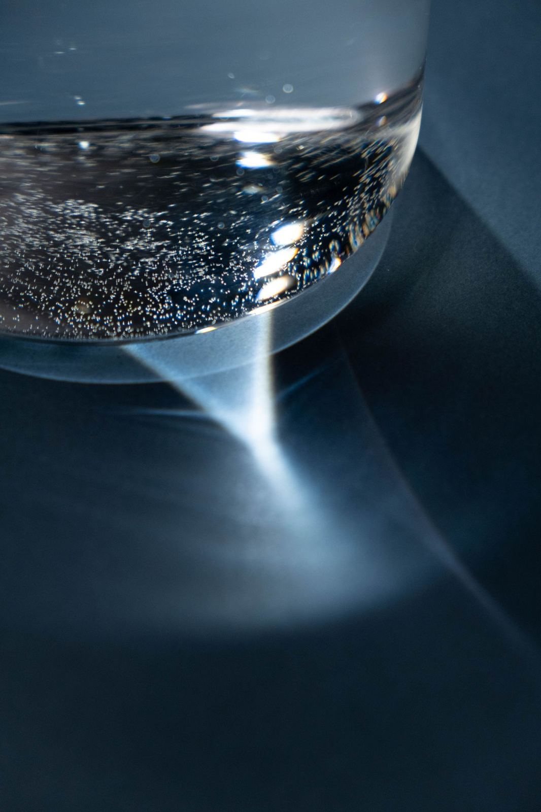 A beam of light passing through a glass bowl on a dark surface.