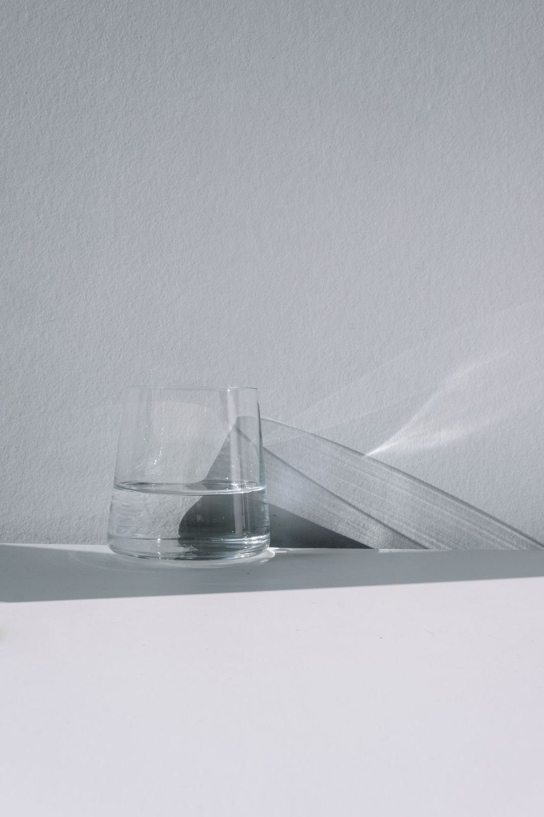 A clear glass and a curved glass pane on a pale shelf.