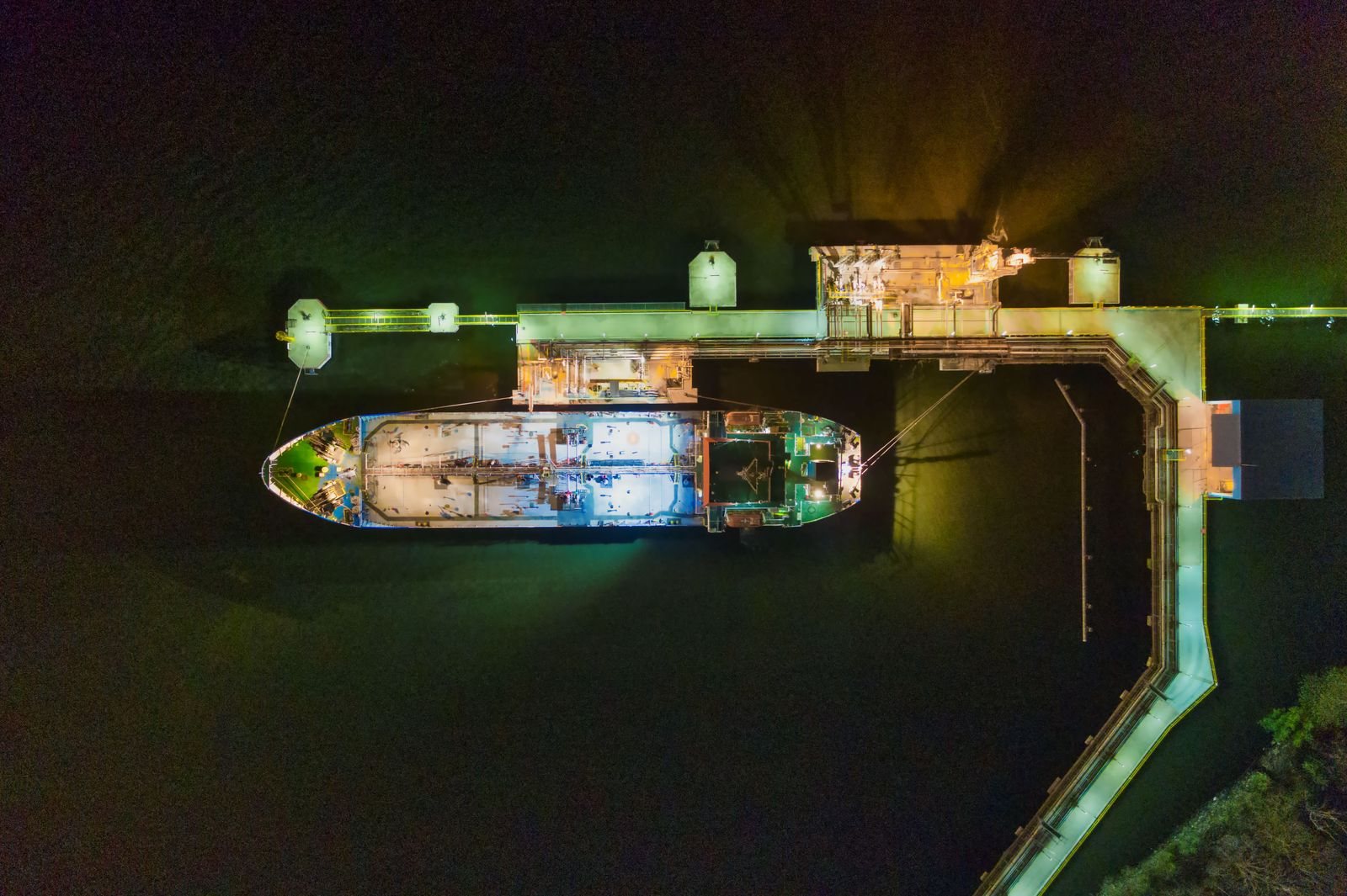 A ship moored at a lit industrial pier at night, seen from above.